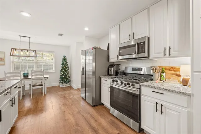 a kitchen with stainless steel appliances granite countertop a stove a refrigerator a sink a stove and white cabinets with wooden floor