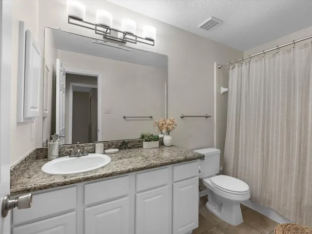 a bathroom with a granite countertop sink a toilet a mirror and shower curtain