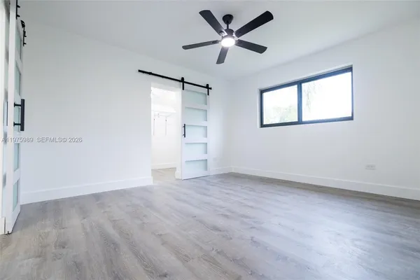 an empty room with wooden floor fan and windows
