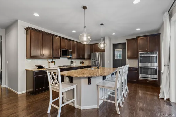 a kitchen with stainless steel appliances kitchen island granite countertop a dining table chairs refrigerator and microwave