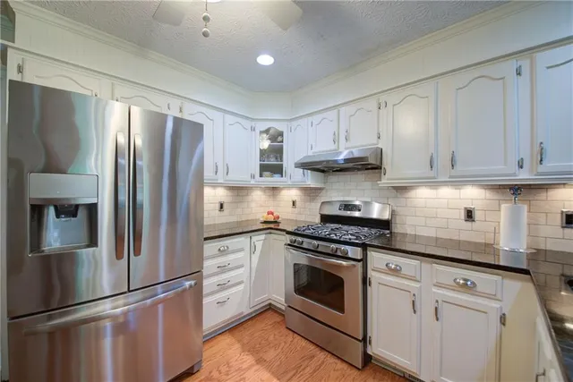 a kitchen with stainless steel appliances granite countertop a stove top oven a sink dishwasher and white cabinets with wooden floor