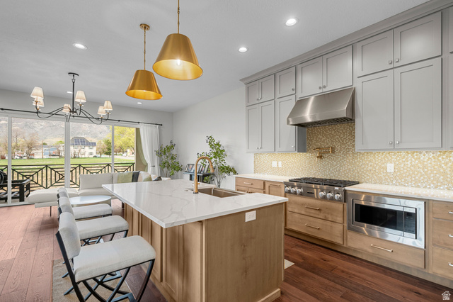 250 South Main Street, Unit 24 Alpine, UT 84004 - Photo 6 of 50 Kitchen featuring light stone countertops, a center island with sink, suspended lighting, stainless steel appliances, and backsplash