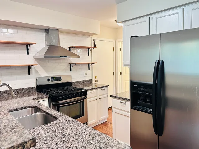 a kitchen with granite countertop stainless steel appliances a stove and a wooden floor