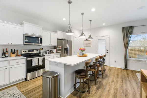 a kitchen with stainless steel appliances a stove a sink a microwave a refrigerator and white cabinets with wooden floor