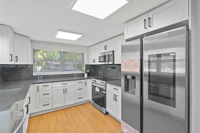 a kitchen with stainless steel appliances granite countertop a refrigerator a sink and white cabinets