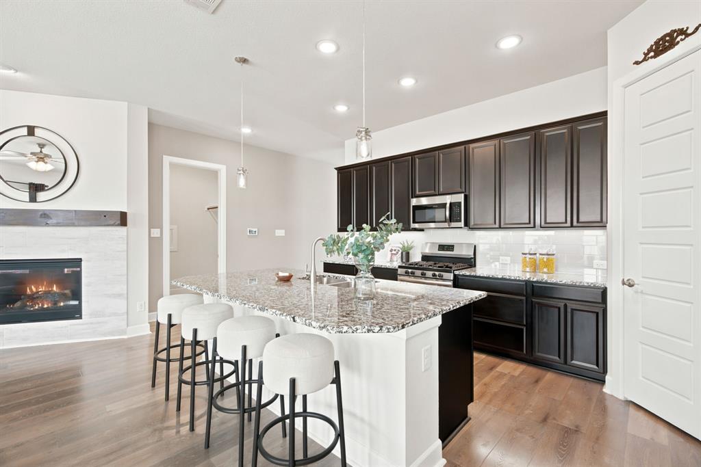 709 Bent Brook Road Oak Point, TX 75068 - Photo 27 of 27 Wood-finish flooring throughout, featuring a kitchen with dark cabinetry, stainless steel appliances, and a central island with a sink