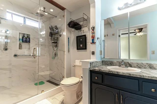a bathroom with a granite countertop sink a toilet a mirror and shower