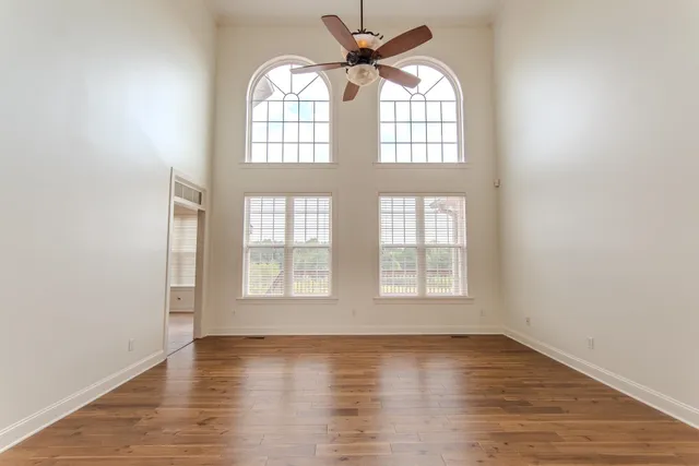 an empty room with wooden floor fan and windows