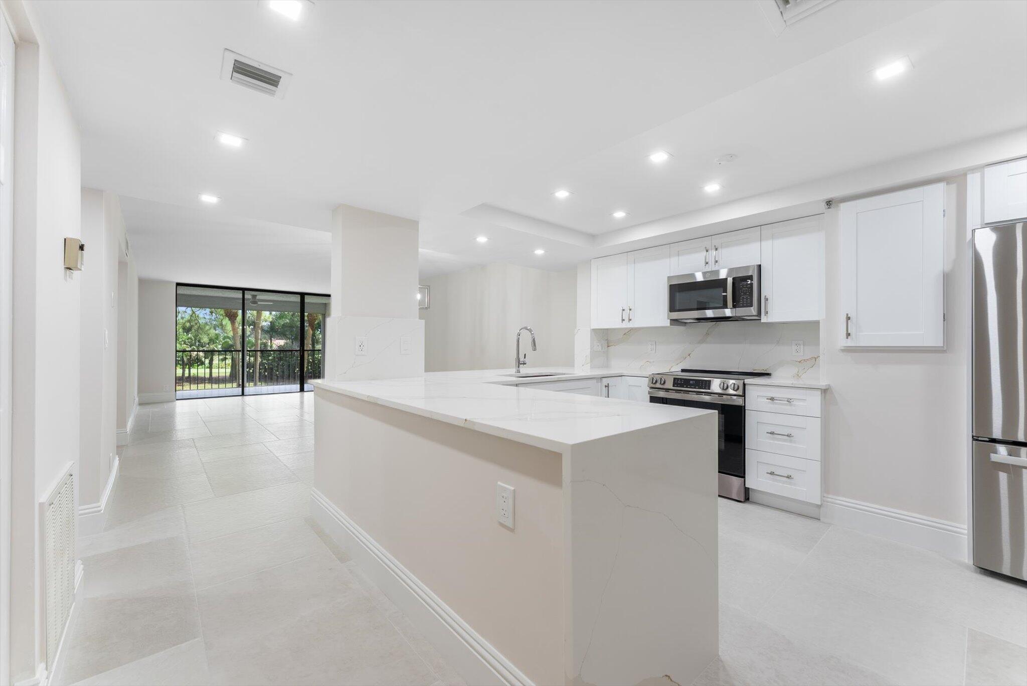 6562 Boca Del Mar Drive, Unit 222 Boca Raton, FL 33433 - Photo 1 of 39 a large white kitchen with stainless steel appliances granite countertop a stove a sink a refrigerator and white cabinets with wooden floor