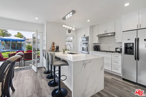 a kitchen with stainless steel appliances kitchen island granite countertop a stove a sink a refrigerator and white cabinets with wooden floor