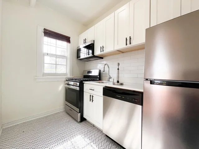 a kitchen with stainless steel appliances a refrigerator a sink and white cabinets