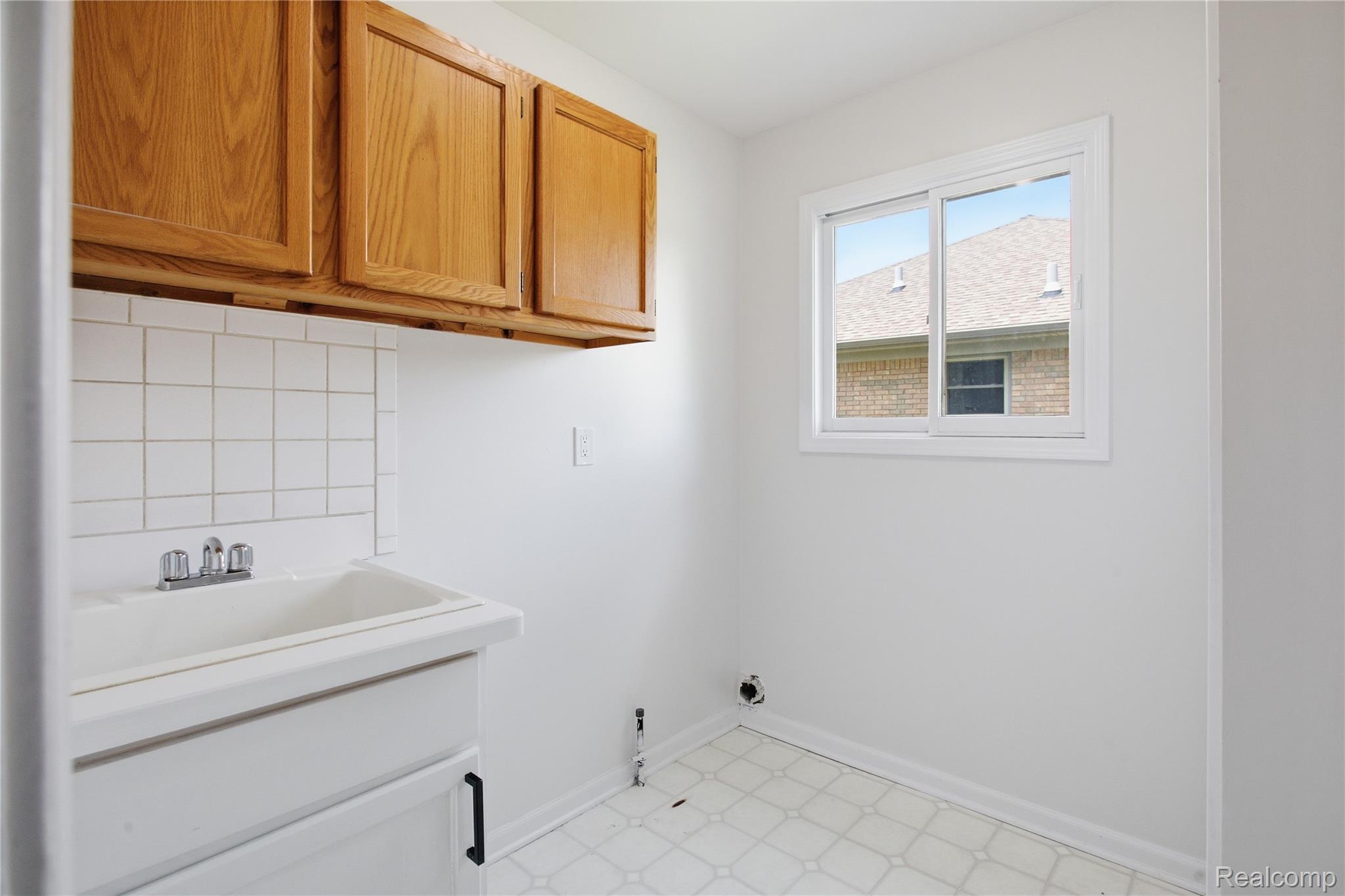 52658 Stag Ridge Drive Macomb, MI 48042 - Photo 15 of 28 Utility room featuring a built-in sink with chrome faucet, white tile backsplash, and light wood cabinetry