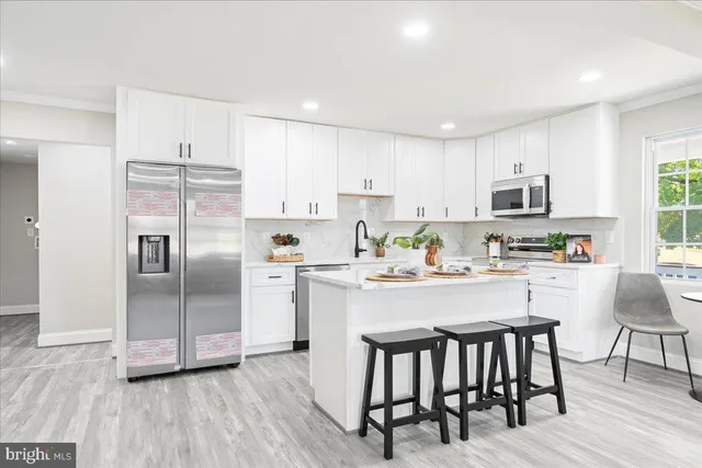 a kitchen with stainless steel appliances granite countertop a stove a sink a microwave a refrigerator and white cabinets with wooden floor