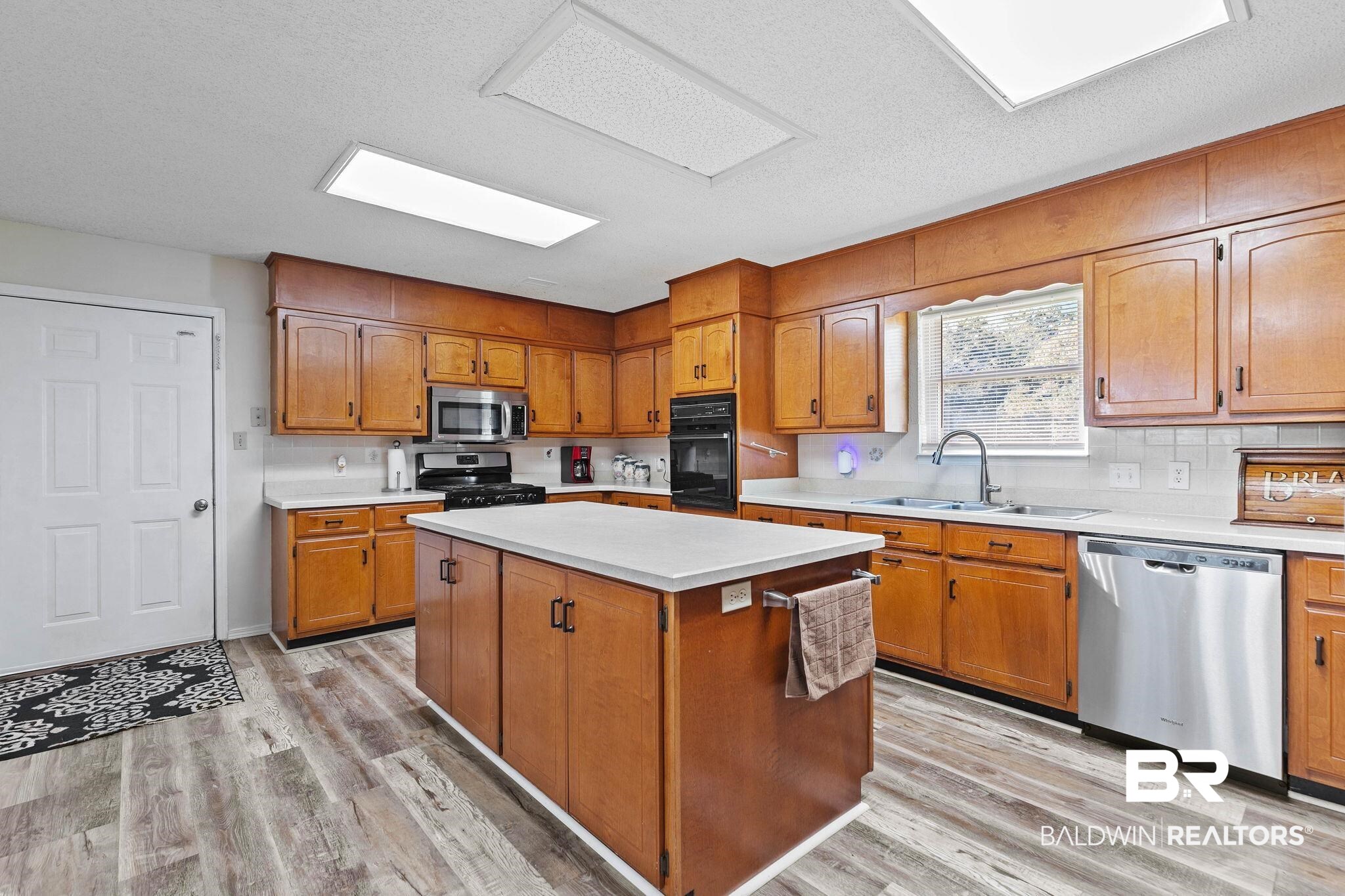 1510 South Juniper Street Foley, AL 36535 - Photo 13 of 36 Kitchen with black appliances, light countertops, brown cabinetry, a kitchen island, and light wood finished floors