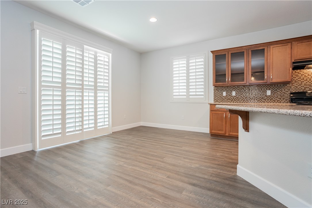 971 Huntington Cove Parkway Las Vegas, NV 89178 - Photo 20 of 55 Kitchen with brown cabinetry, wood finished floors, glass insert cabinets, tasteful backsplash, and under cabinet range hood