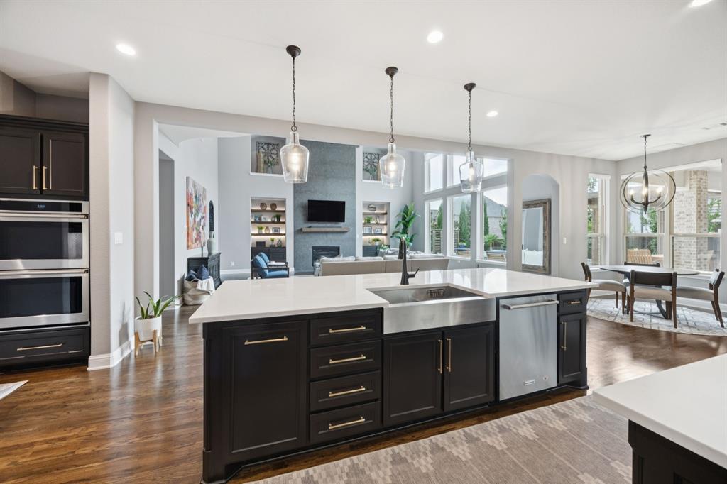 7121 Calypso Lane Frisco, TX 75036 - Photo 10 of 40 a kitchen with stainless steel appliances granite countertop a sink a oven a dining table and chairs with wooden floor