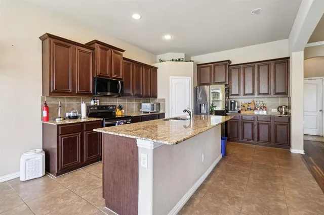 a large kitchen with kitchen island granite countertop a sink a counter top space a stove and a refrigerator