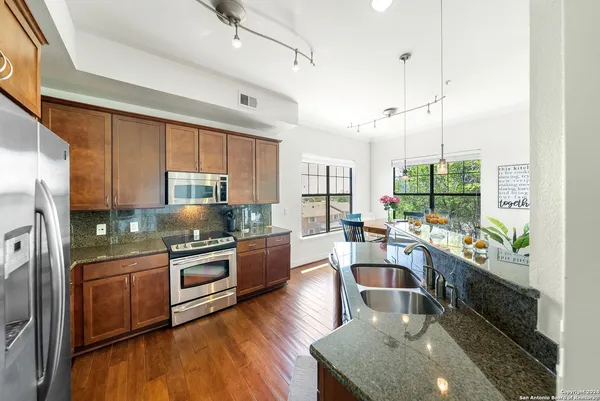 a kitchen with stainless steel appliances granite countertop wooden floors a stove and a refrigerator