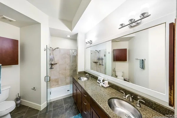 a bathroom with a granite countertop double vanity sink a mirror and a shower