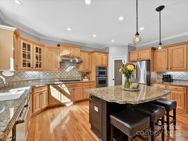 a kitchen with stainless steel appliances granite countertop wooden cabinets a stove top oven a granite counter and chairs