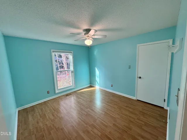 an empty room with wooden floor chandelier fan and windows