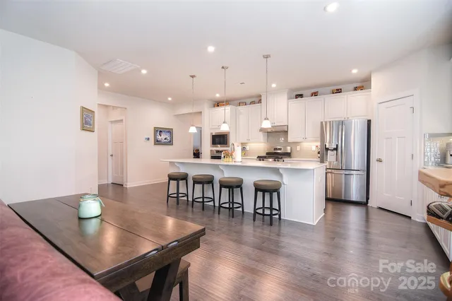 a kitchen with stainless steel appliances granite countertop a stove a refrigerator a kitchen island a dining table and chairs