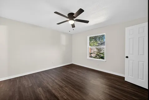 a view of an empty room with wooden floor and a ceiling fan