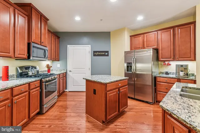 a kitchen with stainless steel appliances granite countertop a refrigerator a stove top oven a sink and dishwasher wooden cabinets with wooden floor