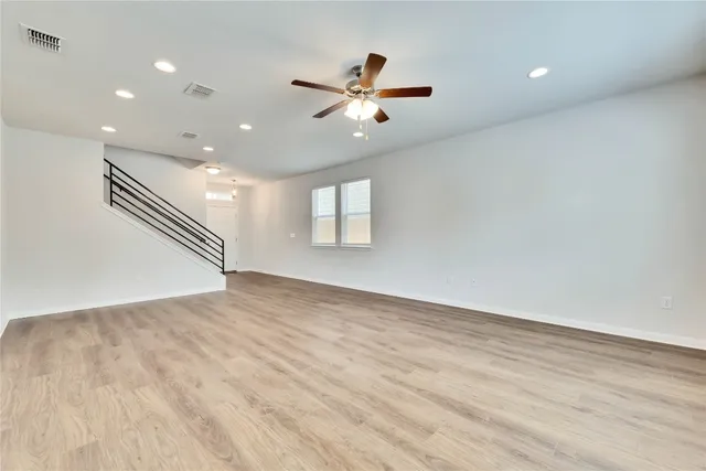 a view of an empty room with wooden floor and a ceiling fan