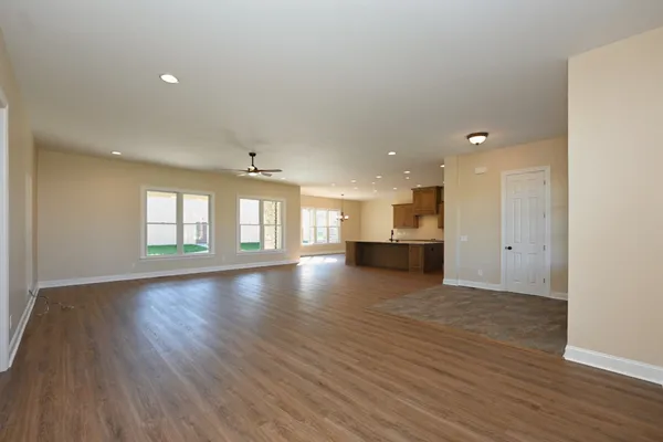 a view of an empty room with wooden floor and kitchen
