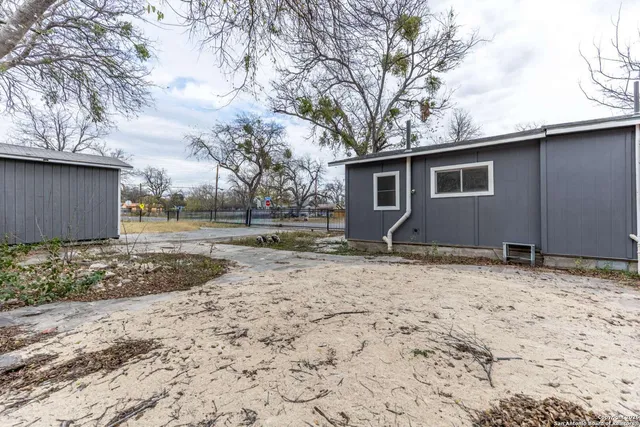 a backyard of a house with large trees and wooden fence