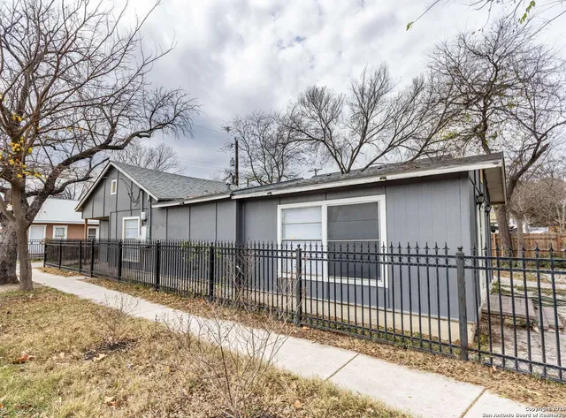 a view of a white house with a large tree and wooden fence