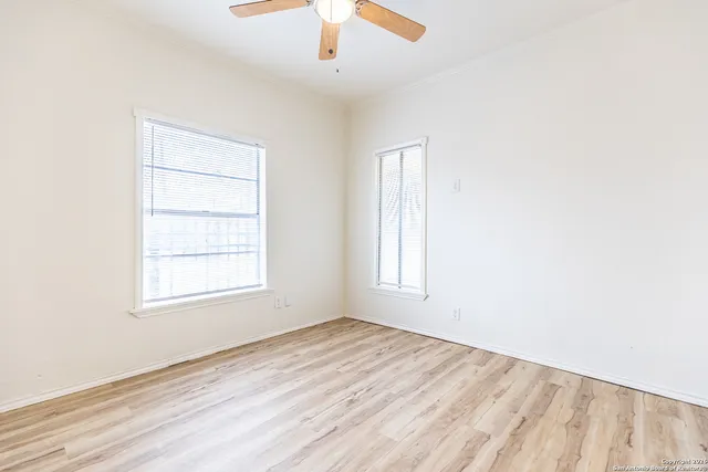 an empty room with wooden floor chandelier fan and windows