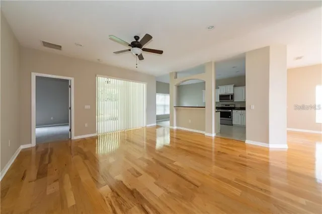 a view of empty room with wooden floor and kitchen view