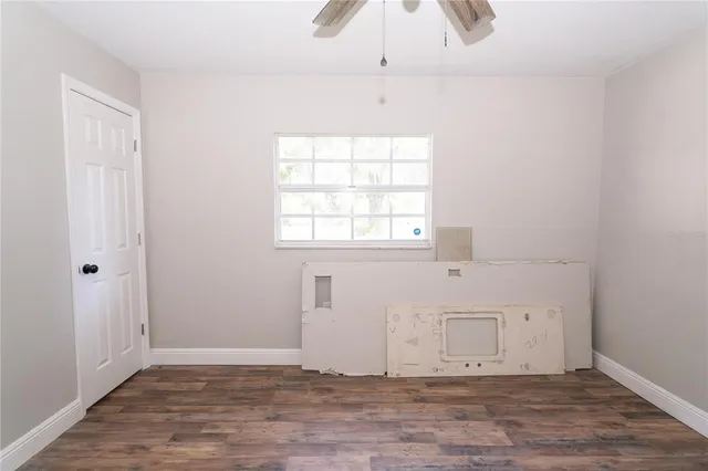 an empty room with wooden floor chandelier fan and windows