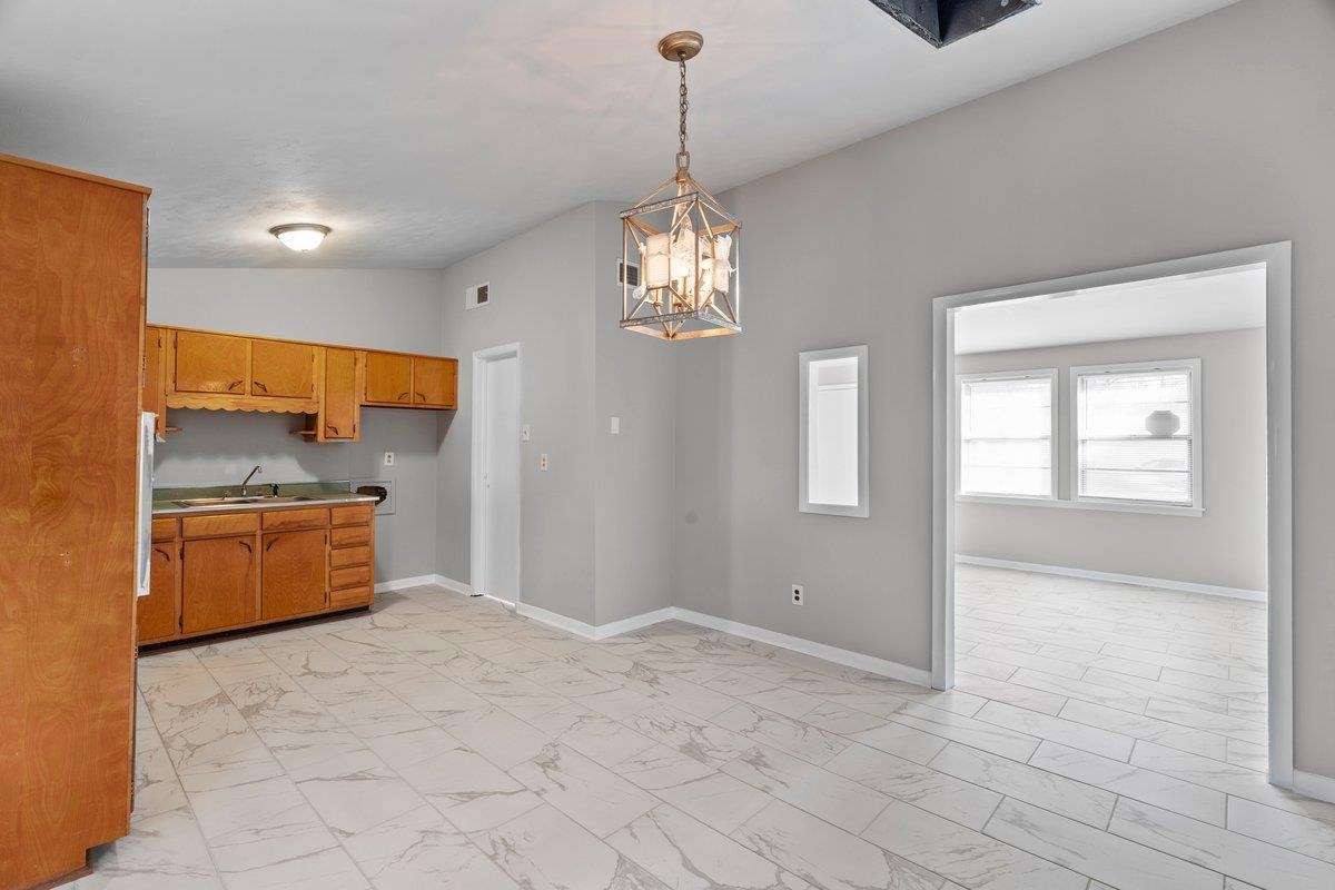 4948 Knight Arnold Road Memphis, TN 38118 - Photo 2 of 27 Kitchen with vaulted ceiling, a chandelier, light marble finish floors, pendant lighting, and brown cabinets