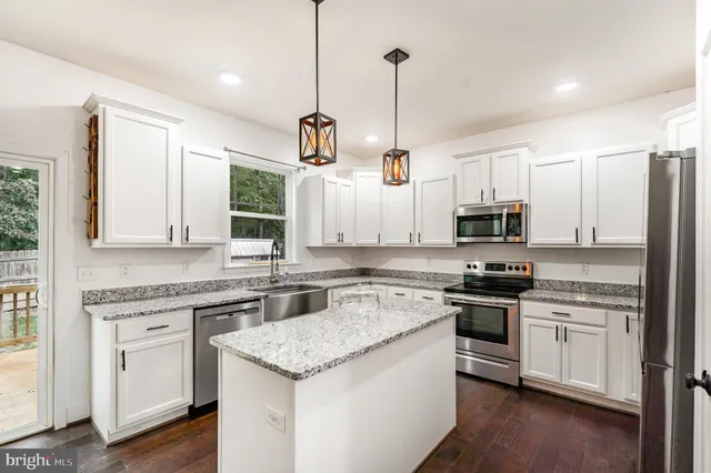 a kitchen with stainless steel appliances granite countertop a stove a sink dishwasher a refrigerator white cabinets and wooden floor next to a window