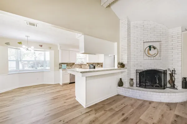 a open kitchen with granite countertop a stove top oven a clock and white cabinets with wooden floor