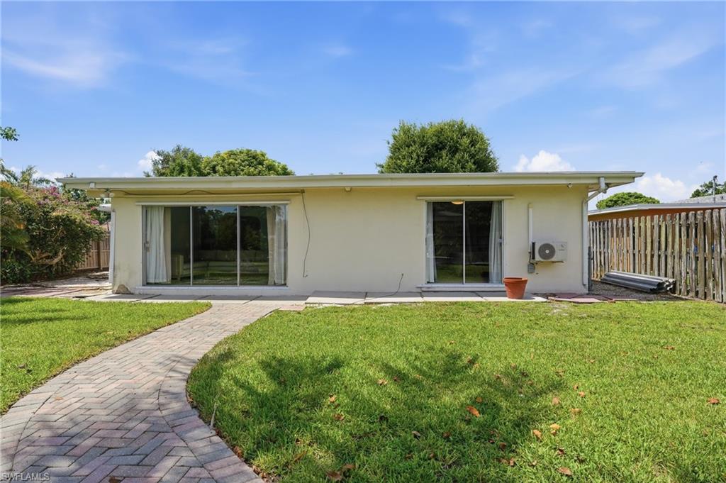 1316 Rordon Avenue Naples, FL 34103 - Photo 32 of 38 Expansive backyard featuring a manicured lawn, a paved brick pathway, and two sets of sliding glass doors