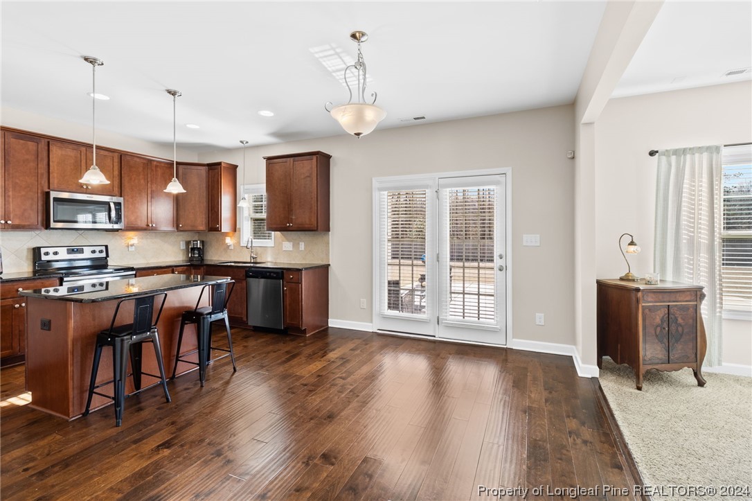 6817 Hunters Den Road Hope Mills, NC 28348 - Photo 16 of 49 a large kitchen with stainless steel appliances granite countertop a stove a sink dishwasher a microwave oven and a dining table with wooden floor