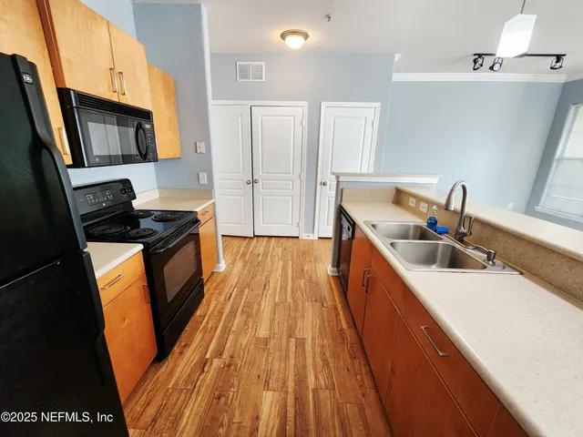 a kitchen with stainless steel appliances a stove a sink a refrigerator wooden floor and cabinets