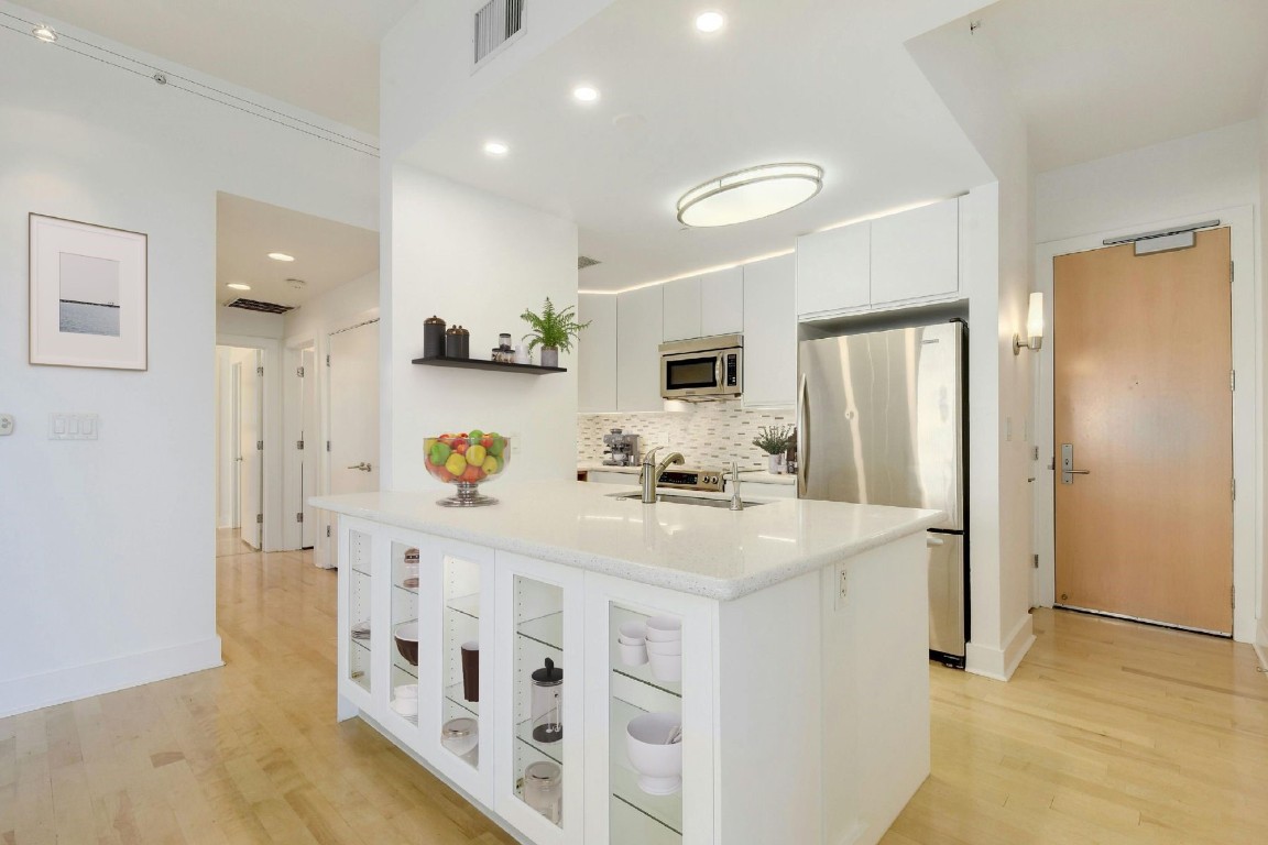 a kitchen with stainless steel appliances a refrigerator a sink dishwasher and white cabinets with wooden floor