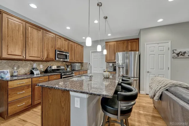 a kitchen with stainless steel appliances granite countertop a stove a sink dishwasher and a refrigerator with wooden cabinets