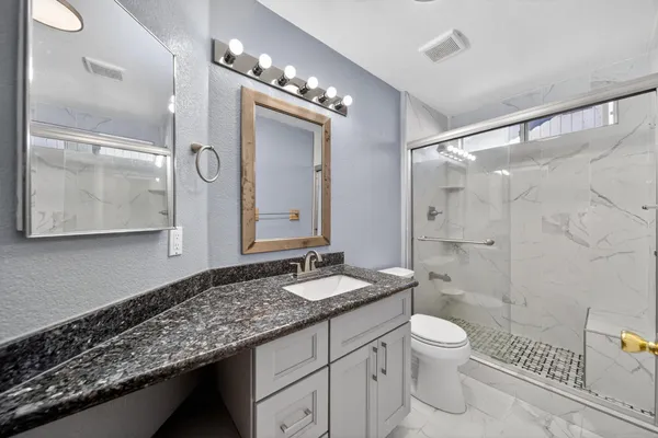 a bathroom with a granite countertop sink toilet a mirror a vanity and shower