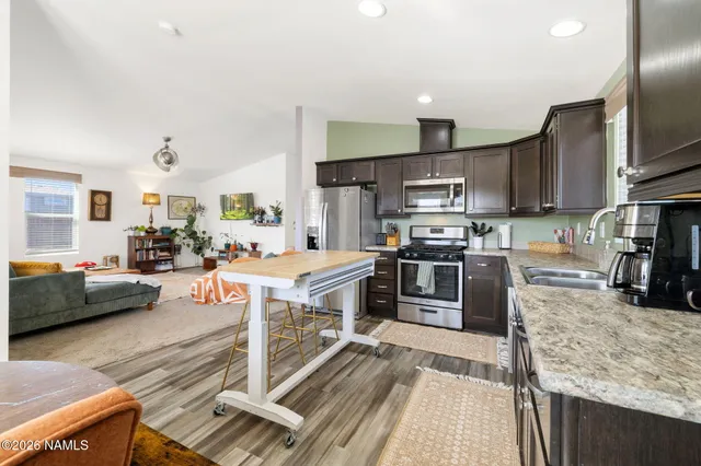 a kitchen with stainless steel appliances granite countertop a stove top oven a sink dishwasher a dining table and chairs with wooden floor