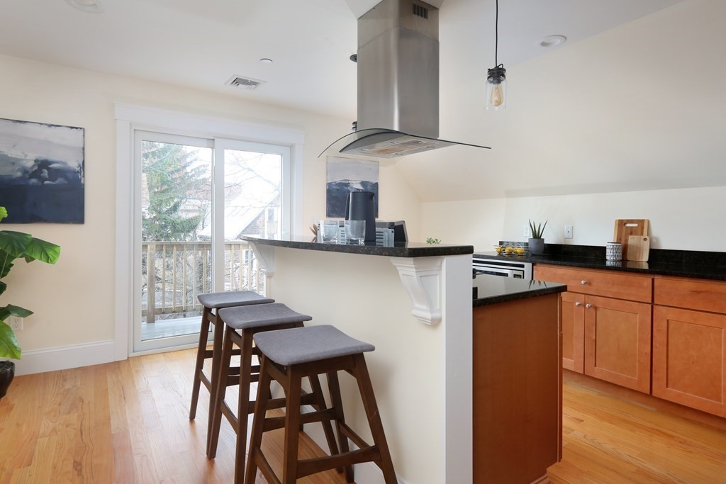 150 Lowell Street, Unit 3 Somerville, MA 02143 - Photo 2 of 12 a kitchen with stainless steel appliances kitchen island a table chairs in it and wooden floors