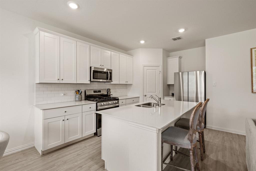3200 Willow Terrace Lane Anna, TX 75409 - Photo 21 of 40 a kitchen with a sink a stove a refrigerator and white cabinets with wooden floor