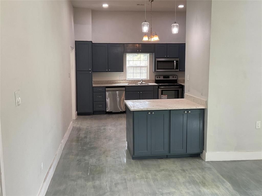 207 College Street Chico, TX 76431 - Photo 10 of 20 Kitchen featuring appliances with stainless steel finishes, a chandelier, decorative light fixtures, a peninsula, and light stone counters