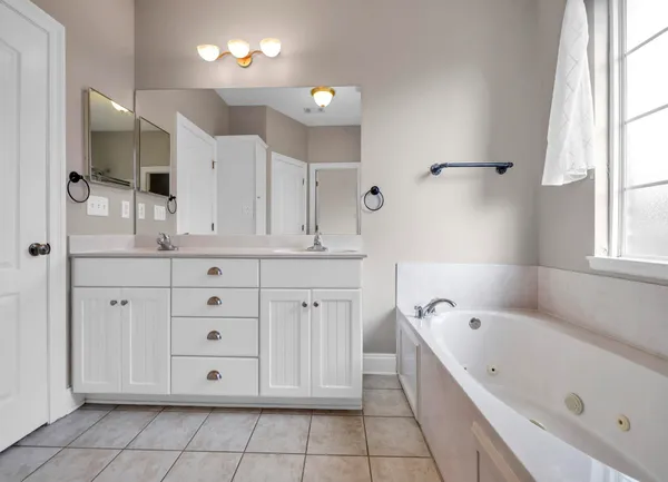 a bathroom with a bathtub a double vanity sink a vanity a window and a mirror
