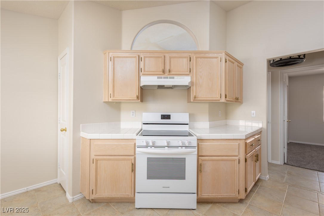 490 Ruby Drive Mesquite, NV 89027 - Photo 12 of 23 Kitchen featuring light brown cabinetry, white range with electric cooktop, tile countertops, under cabinet range hood, and light tile patterned floors